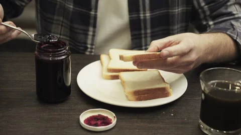 Young man eating a fresh slice of bread with jam for breakfast. Slow motion 스톡 동영상 274385033