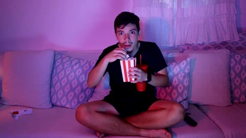Young man eating popcorn while watching a movie at home Stock Footage 289732295