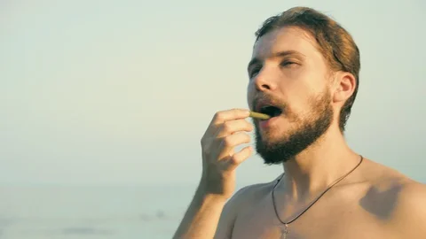 Young man eating snacks on beach Stock Footage 125718906