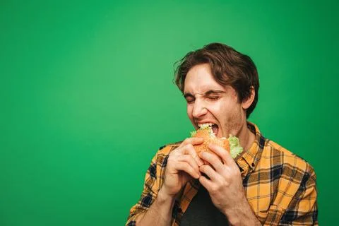 Young man eats burger with pleasure, isolated on green background Stock Photos