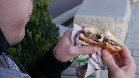 Young Man eats a Cheeseburger from a Burger King on a Street Stock Footage 142765022