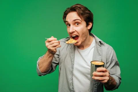 Young man eats corn in a jar, isolated on green background Stock Photos