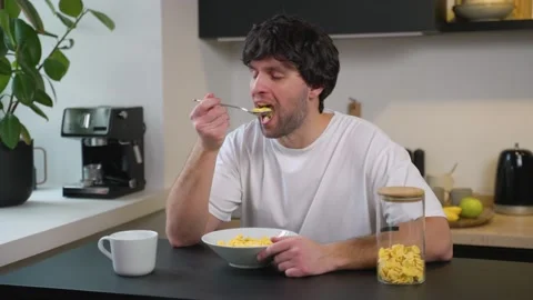 Young man eats cornflakes for breakfast at the table in the kitchen at home Stock-Footage 235921799