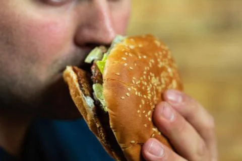 Young man eats delicious appetizing burger. Stock Photos