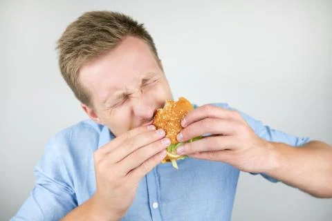 Young man eats fresh tasty burger from fast food restaurant looks very hungry on Stock Photos