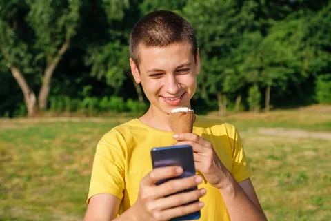 Young man eats ice cream and use smartphone outdoors Stock Photos