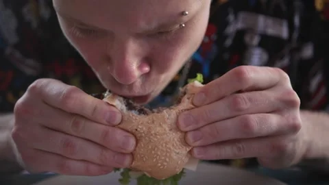 Young man eats meat burger with pleasure, bites burger with his mouth, man eats Stock-Footage 233765475