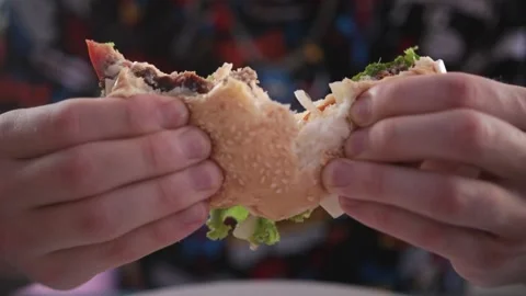 Young man eats meat burger with pleasure, breaks a burger into 2 halves. slow Stock-Footage 233765588