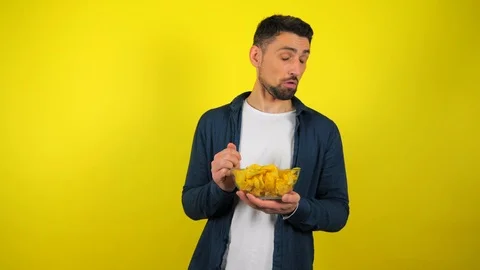 Young man is eats not tasty chips from transparent glass plate and don't like it Stock Footage 119864122