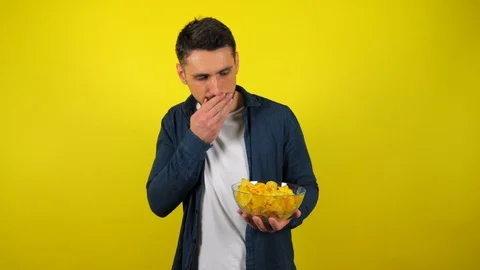 Young man is eats not tasty chips from transparent glass plate and don't like it Stock Footage 119864476