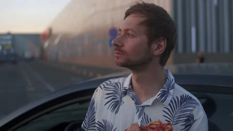 A young man eats pizza with gusto in the parking lot Stock Footage 229570994