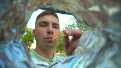 A young man eats potato chips from a packet while walking in the park. View of a Stock Footage 250203441