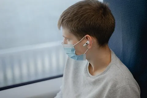 A young man eats in a public place looks out the window, in a medical mask, l Stock Photos