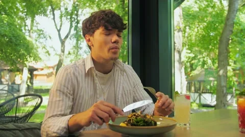 Young man eats at a restaurant. Young couple dining in a cafe against a back Stock Footage 202479317