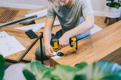 A young man with an electrical screwdriver assembles a tv stand console Stock Photos