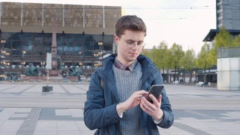A young man with an electronic gadget on the central square of a European city Stock Footage 80736401