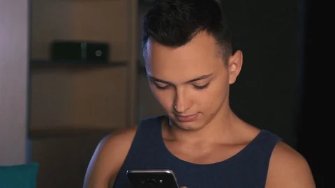 A young man emotionally writes a message on a smartphone, a dark background, a Stock Footage 94652154