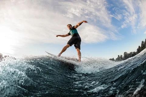 Young man energetically balancing on wave on wakesurf board on splashing wave. Photos