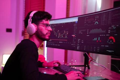 Young man engaged in data analysis while using dual monitors in a cozy, col.. Stock Photos