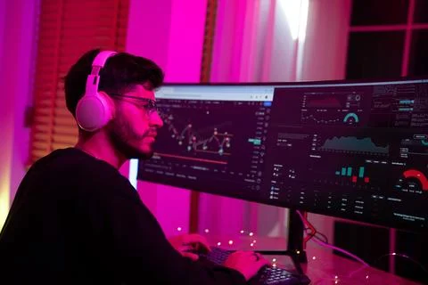 Young man engaged in data analysis using dual monitors in a cool-toned, amb.. Stock Photos