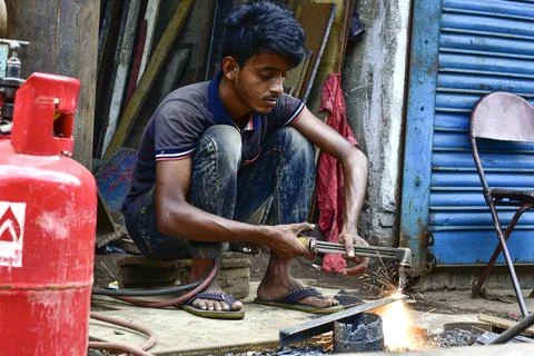 Young man engaged in metalworking using a torch in a workshop. Stock Photos