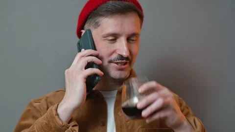 A young man is engaged in a phone conversation while holding a glass in one hand Stock Footage 337643329