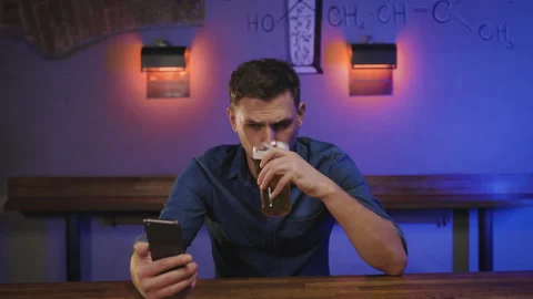 A young man is engaged in a video call while sitting at a bar. He holds his Video stock 286814686