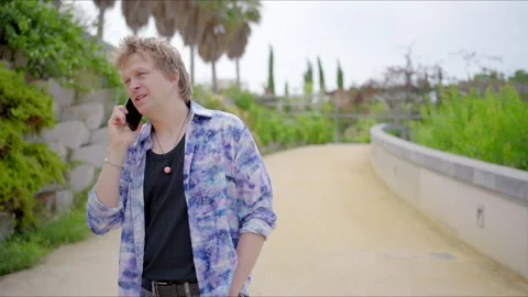 A young man engaging in a phone conversation while enjoying nature in a vibrant Stock Footage 281608402