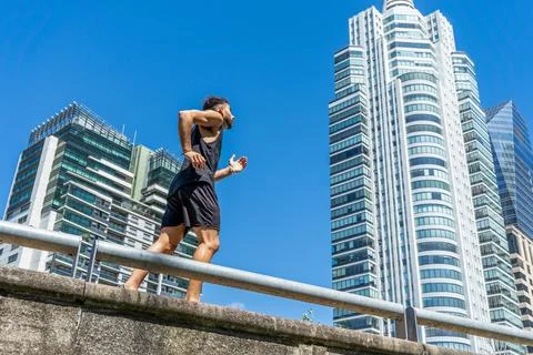 Young man engaging in a refreshing run along a city sidewalk Stock Photos