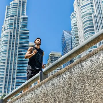 Young man engaging in a refreshing run along a city sidewalk. Stock Photos