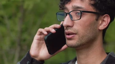 Young man engaging in a smartphone conversation amidst lush outdoor scenery Stock Footage 287708799