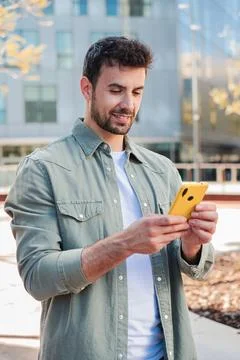 Young man engaging with smartphone while enjoying sunny day outdoors in vibrant Fotos Stock