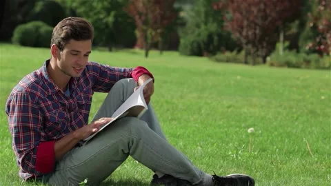 Young man engrossed in a book while sitting on lush green grass Stock Footage 311659166