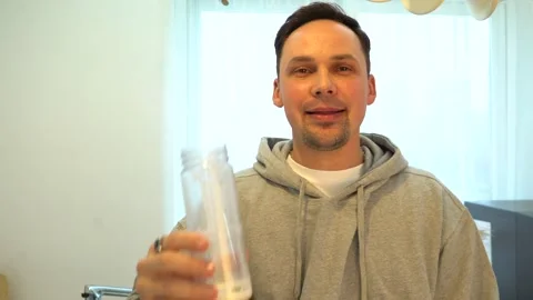 Young man enjoying a protein shake at home, smiling and relaxed. Healthy Stock Footage 326130063