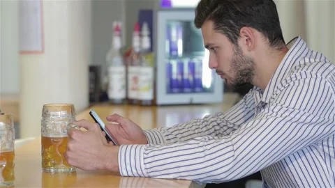 Young man enjoying a refreshing beer while checking his phone Stock Footage 311539461