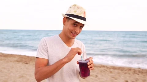 Young man enjoying a refreshing drink on the beach Stock Footage 310185490