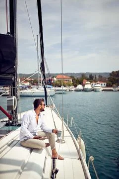 A young man is enjoying a view while sitting on a yacht at sea and using a ta Stock Photos