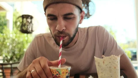 A young man enjoys a refreshing drink through a striped straw while sitting in a Stock Footage 342545093