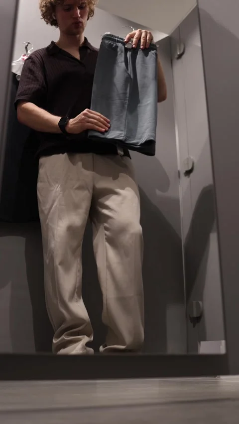 Young man enjoys the soft material of shorts while shopping in a fitting room Stock Footage 344855888