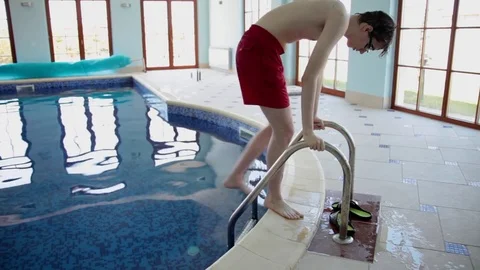 Young man entering swimming pool by a ladder leaving flip-flops behind Stock Footage 69784575