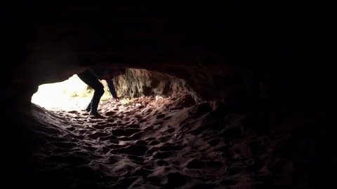 Young man enters dark cave chamber under low stone vault and walk into darkness Stock Footage 80053622