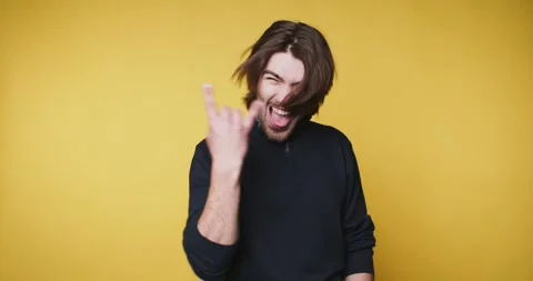 Young man enthusiastically makes a rock gesture on yellow background, embod.. Stock Footage 314336949