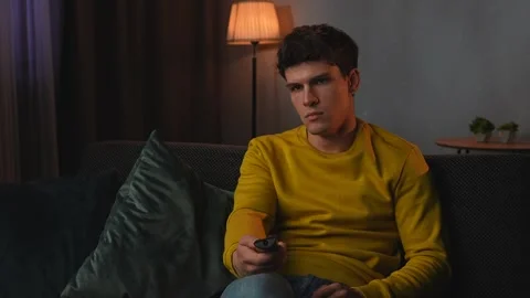 Young man in the evening after work relaxing at home, sitting on the sofa in Stock Footage 300039525
