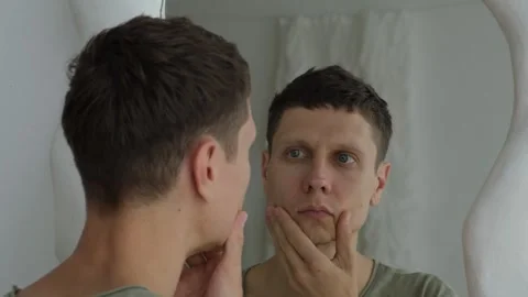 Young man examines face in mirror, checking for wrinkles. Self acceptance Stock-Footage 311048479