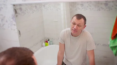 Young man examines his reflection in the mirror while standing in the bathroom Stock Footage 141213070