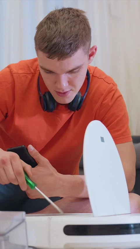 Young Man Examines Tech Device with Screwdriver and Smartphone in Indoor Setting Stock Footage 346790403