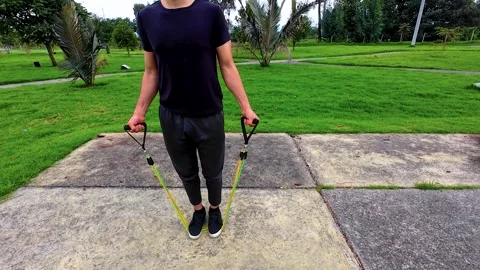 Young man exercising with elastic arm bands in a park workout Stock Footage 275722352