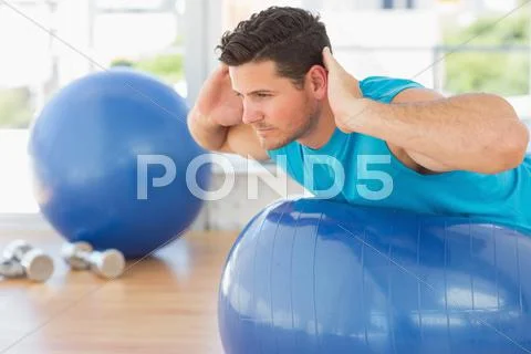 Young man exercising on fitness ball at a bright gym Stock Photos