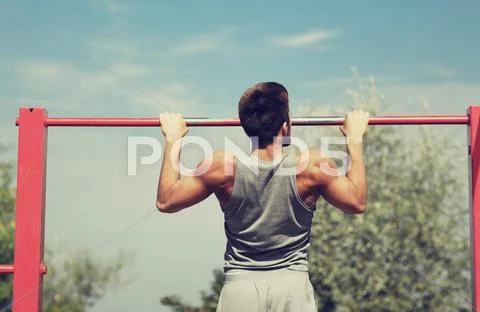Young man exercising on horizontal bar outdoors Stock Photos