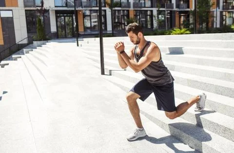 Young man exercising outside. Guy holding hands together and doing squat Stock Photos